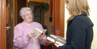 Una voluntària dona un llibre a una dona anciana a la porta de casa seva