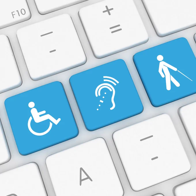 A computer keyboard with three blue keys featuring white accessibility symbols: a person using a wheelchair, a person with hearing loss, and a person using a cane. These symbols represent accessibility for people with physical, hearing, and visual disabilities.