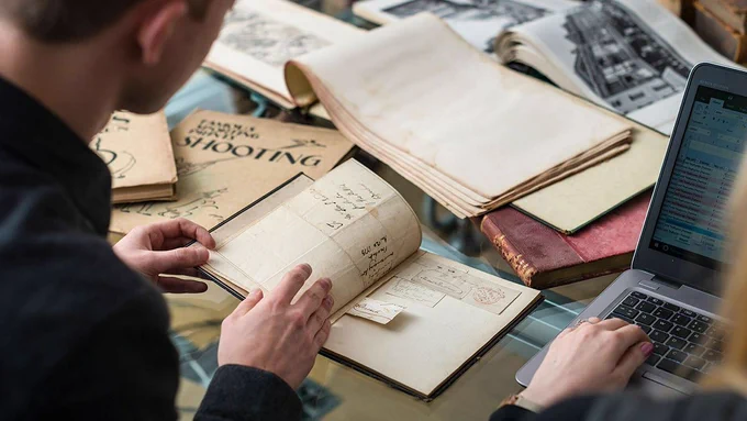 Researchers review special collections materials, vintage books and manuscripts while entering data into a laptop computer.