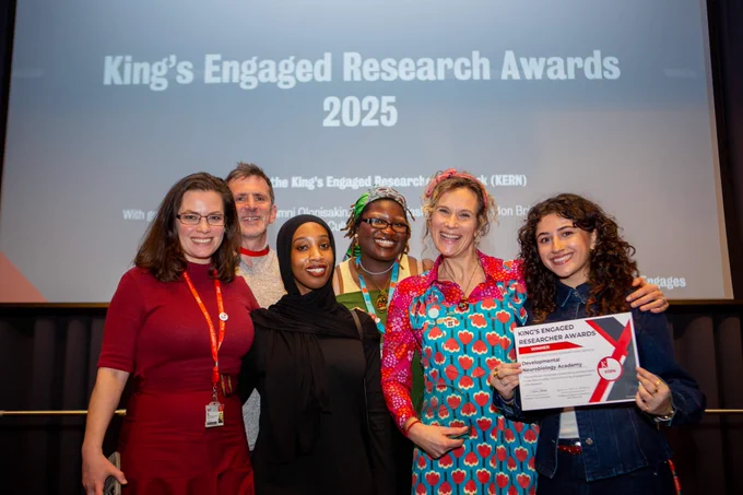 Diverse group of five women and one man holding an award in front of a projector screen.
