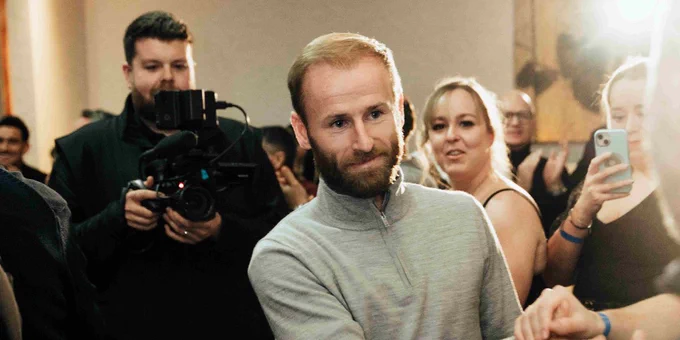 Barry Bannan walks through a crowd of fans. Behind him a man with a camera rig films him.