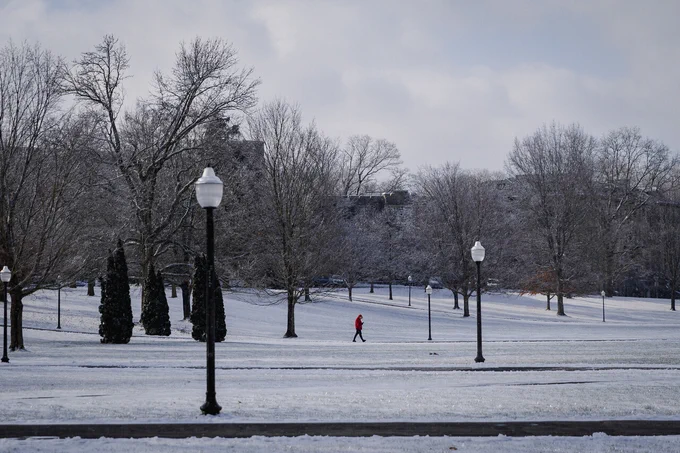 A lone person in a red jacket walks across a snow-covered Drillfield