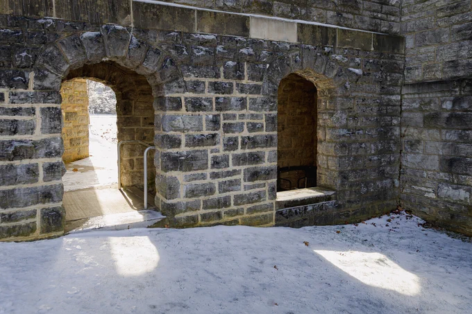 Sunlight shines through Hokie Stone arches onto a snowy lawn