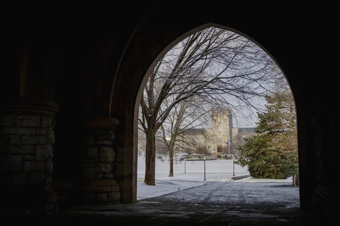A view through an archway of the Drillfield and Burruss Hall with snow coating the ground