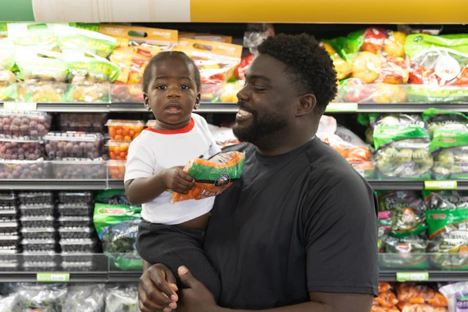 A man holds a child in the produce section of a grocery store.