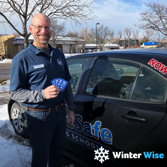 Man holding up blue "Check Your Tread" cards in front of a black DriveSafe vehicle with snow on the ground. The Winter Wise logo is in the bottom right corner.