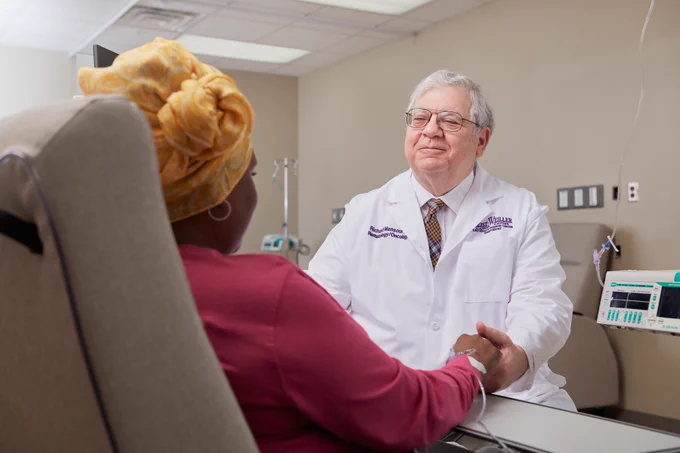 Dr. Richard Mansour wearing his white coat holding the hands of one of his patients in his clinic.