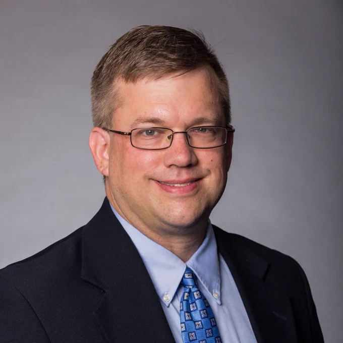 Portrait of Dr. Mark Hoffman wearing a dark suit and a blue tie, smiling at the camera.