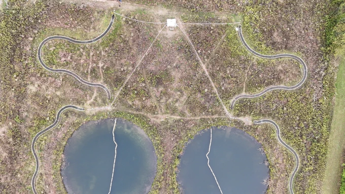 Two bodies of water, both circles, sit against green and brown grass, with white and gray imprints of lines and swirls in the ground around them. At the top of the frame, a white box sits, connected to the water by lines of a triangle.