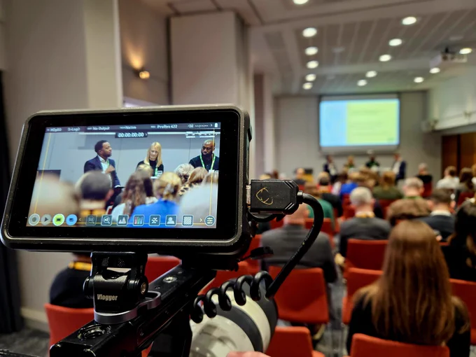A photo of a video screen showing the filming of a conference room.