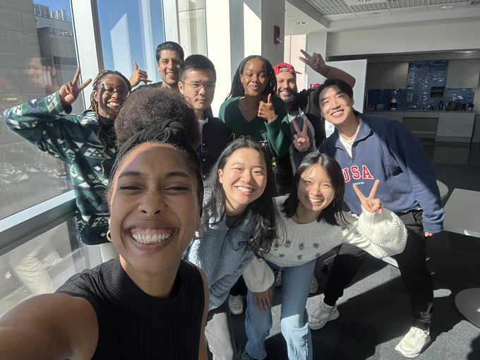 Brielle is pictured in a selfie with her lab standing behind her smiling. Some are holding up peace signs or thumbs up and the sun is shining on them brightly. 