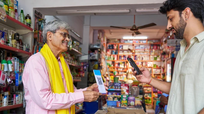 photo from Canva of a small shopkeeper showing the QR code for his customer to make payment via his mobile phone