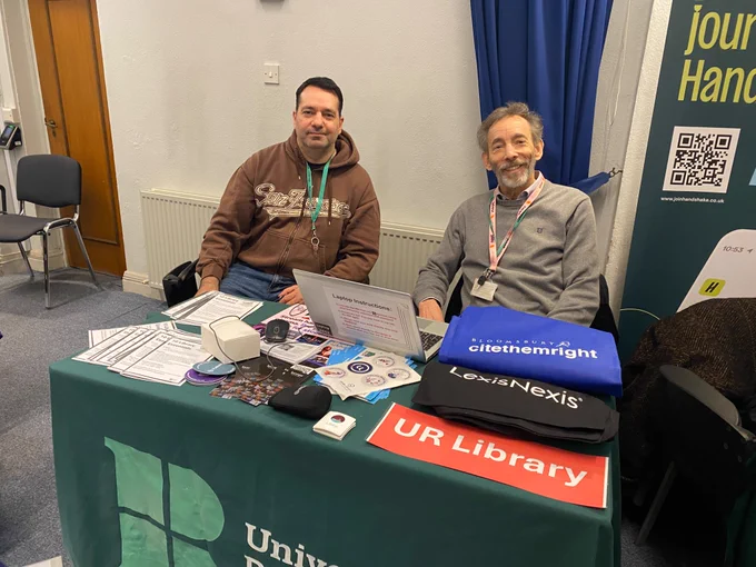 Image shows 2 male staff on the library stall
