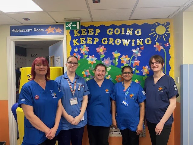 Group of five paediatric nurses in blue uniforms smiling at the camera.