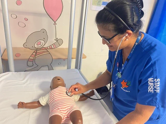 Paediatric nurse wearing a stethoscope checking the heartbeat of a manikin baby.