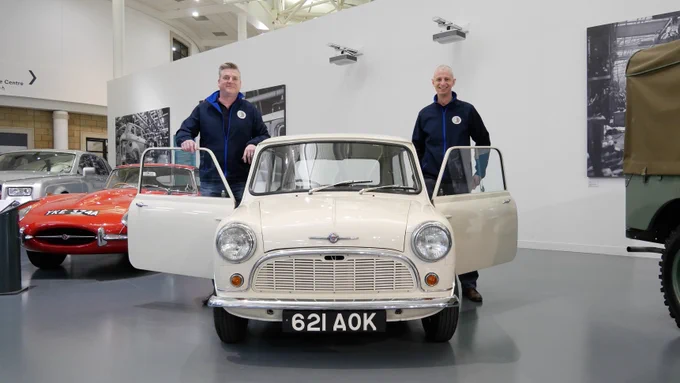 Two representatives of Peter James Insurance standing with the first Mini, at the British Motor Museum.