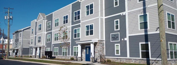 a photo of an apartment building of three stories, clad in dark and light gray with a blue door. 