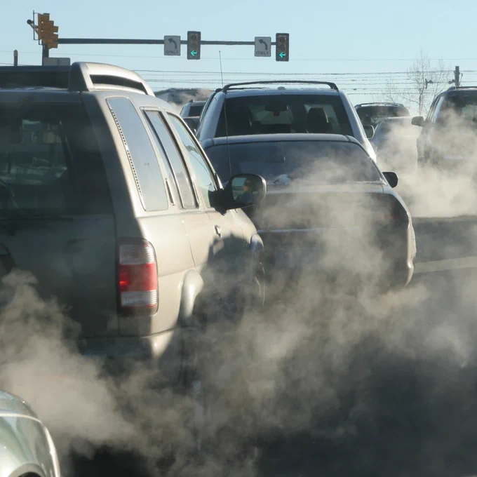 Photo of several cars in traffic with exhaust visibly polluting the air.