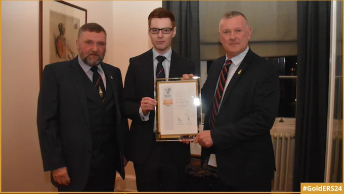 IED Training Solutions's Managing Director and Consultant standing on either side of the Commanding Officer of HMS Scotia, with two of them holding the Gold Award revalidation certificate.