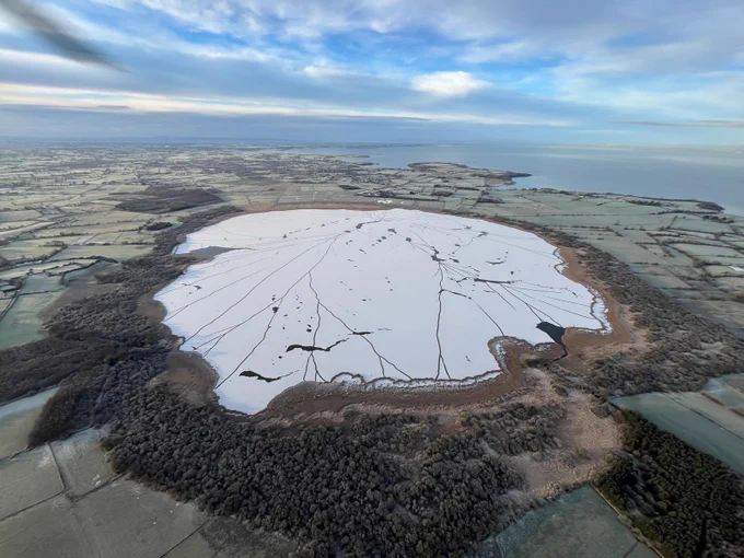 An image of Portmore Lough covered in ice with frosty fields surrounding it