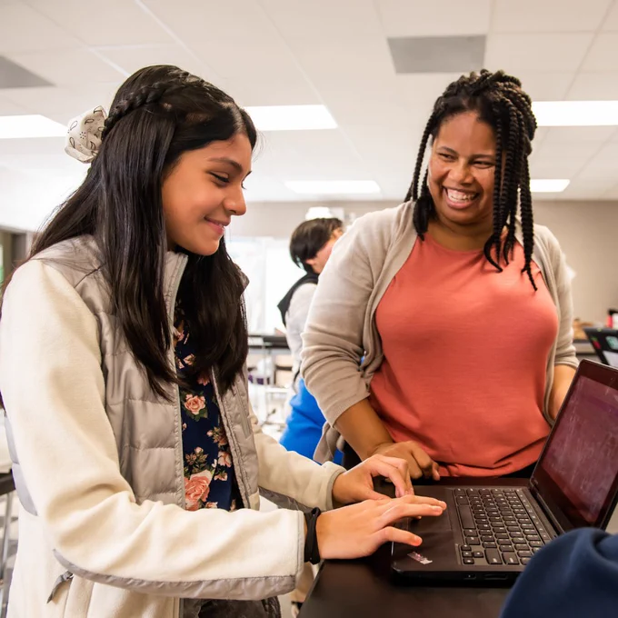 Photo of a young person working on a laptop, accompanied by an educator.