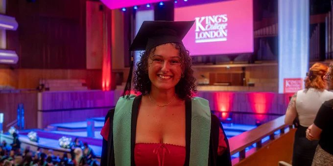A graduate wearing a cap and gown smiles brightly at the camera.