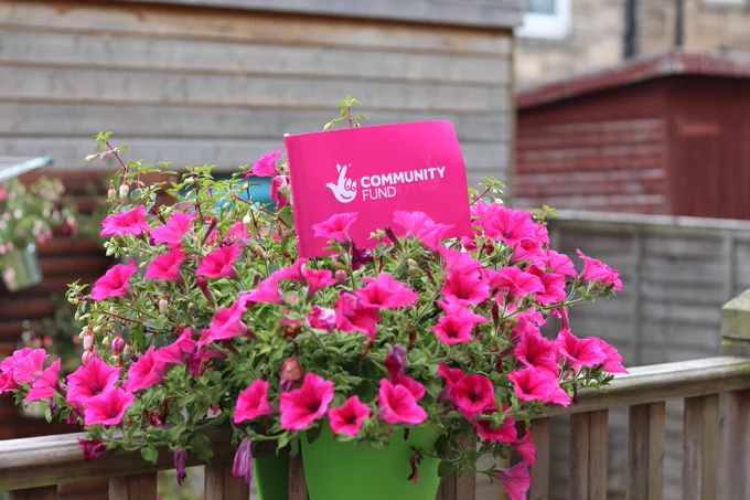 A branded Community Fund flag in a put of pink flowers.