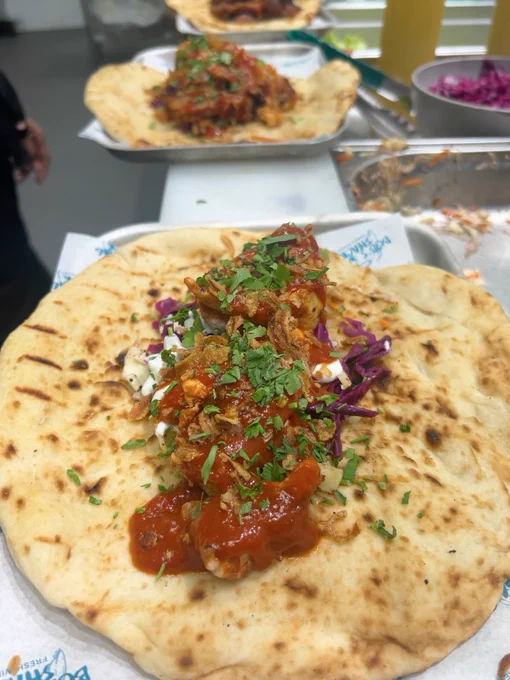 Freshly prepared kebabs topped with herbs and sauces on top of a slice of naan bread. 