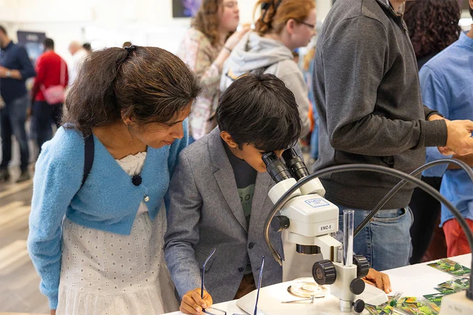 A boy looking through a microscope standing next to a woman at the University of Reading Community Festival. There are people of all ages in the background.