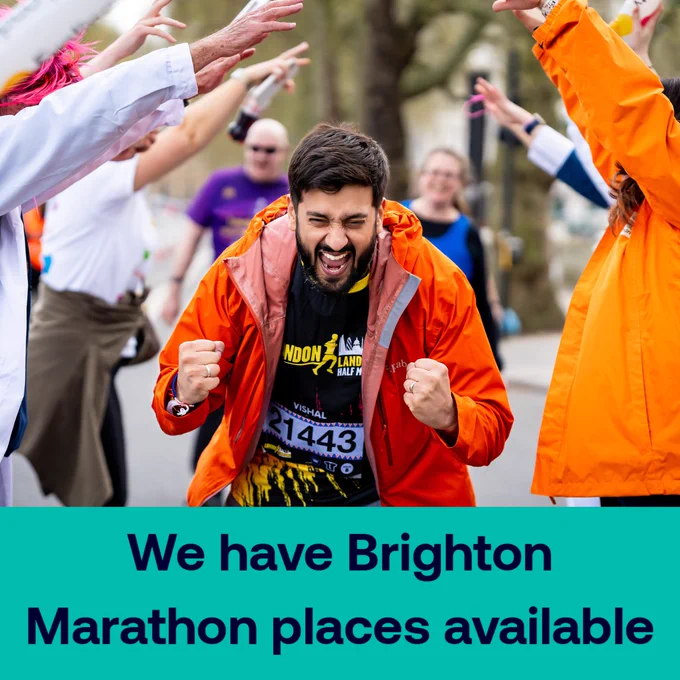 A marathon runner, surrounded by supporters, cheering with clenched fists. They're wearing an orange jacket and a black shirt. There is a teal banner at the bottom of the image with 'We have Brighton Marathon places available' written in navy blue writing. 