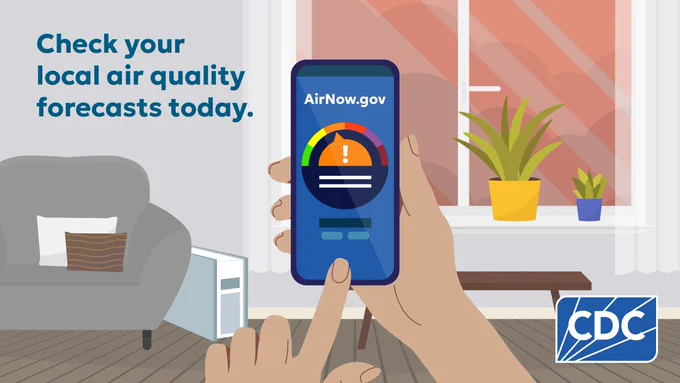 A hand holding a smartphone with the AirNow.gov app open displaying the local air quality scale. Background shows a living room with a chair, window and house plants. Text reads: "Check your local air quality forecasts today."