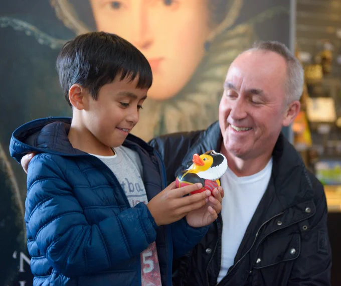 Little boy and a man smile at a rubber duck in the boy's hands. 