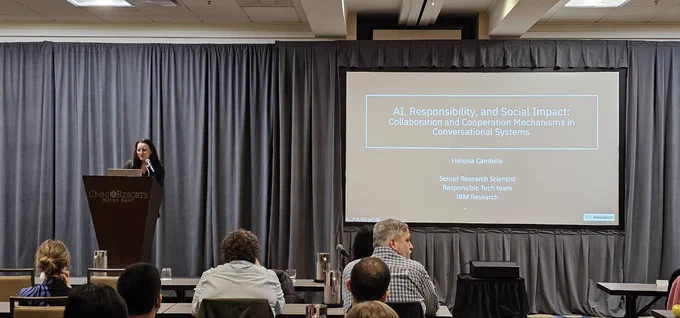 Heloisa Candello presenting her work on a screen at the GROUP Conference, a group of people sitting in front of her.