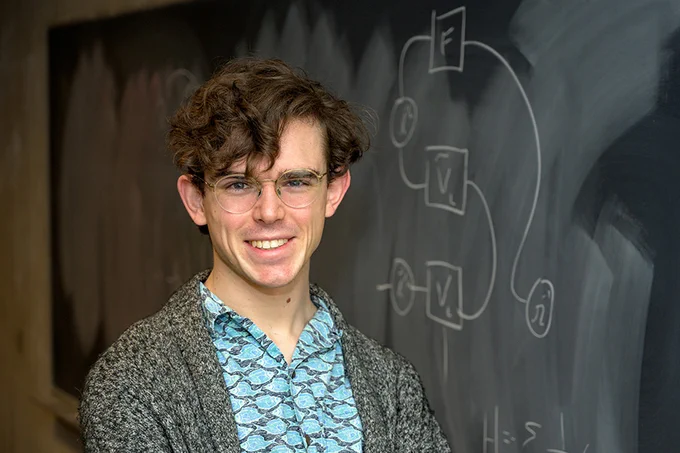 Rokas Veitas stands in front of a blackboard and smiles at the camera.