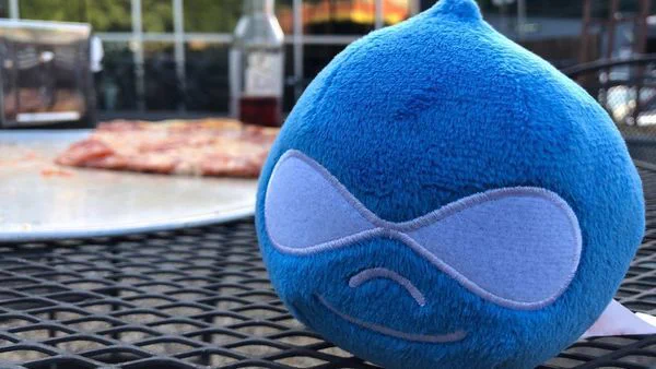 Small Drupal drop stuffy on a table with pizza in the background.