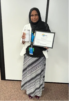 Person standing indoors, holding a glass trophy and a certificate from 'GEC', smiling at the camera.