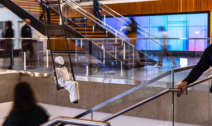 Art installation "Not Afraid of Falling" by Glenn Kaino, featuring a small automaton robot dressed in white sitting on a swinging trapeze