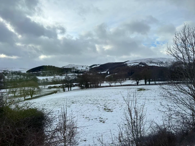 The view of a snowy field out of the window of a train. Chunky snow with the mountains in the background