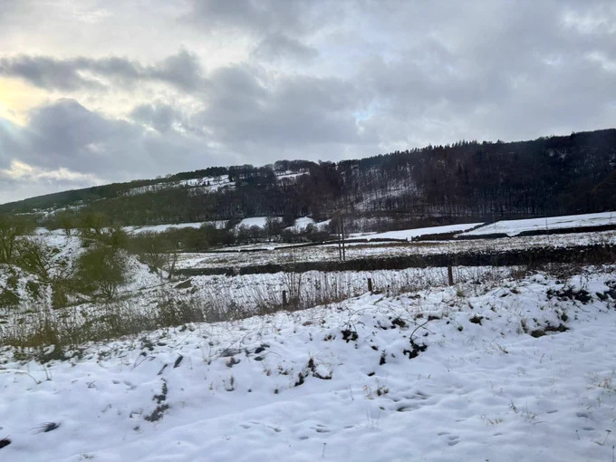 The view of a snowy field out of the window of a train. Chunky snow with the mountains in the background