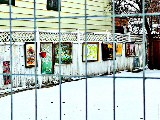 Framed artworks attached to wooden fence behind metal fence