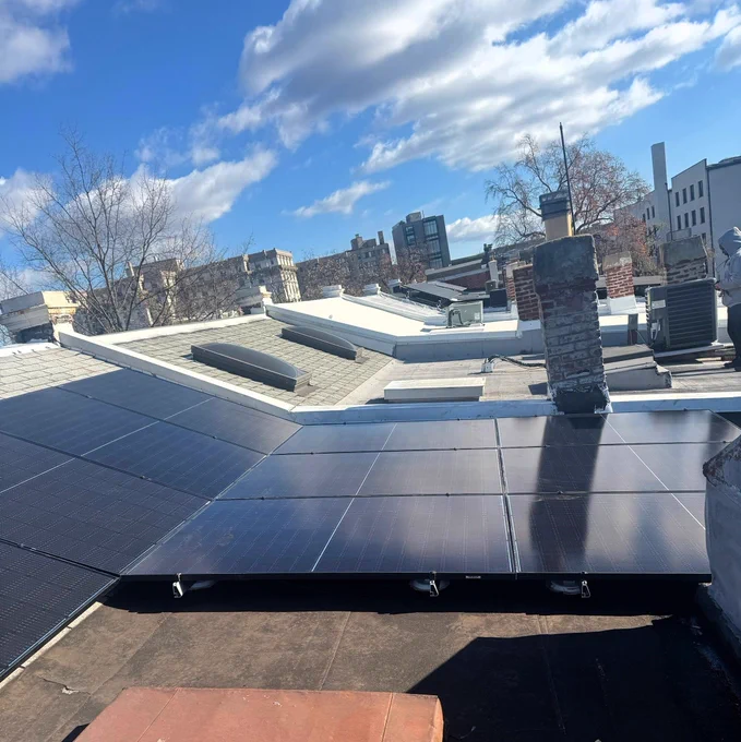 A solar array on a flat roof under a blue sky with gray and white clouds.