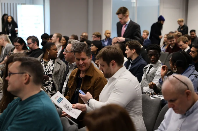 In a crowded room, two attendees engage with a QR code at Venturefest West Midlands 2024.