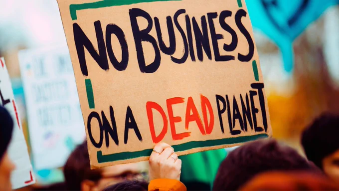 Person holding a sign saying 'No Business on a Dead Planet'.