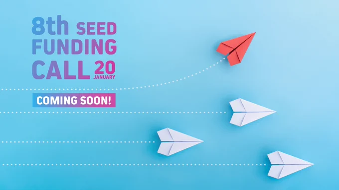 The image shows a blue background with a pattern of dotted lines, suggesting movement. Three white paper planes and one red paper plane symbolise progress and innovation, with the red plane leading the way. The text is prominently displayed in gradient shades of purple and pink: “8th Seed Funding Call – 20 January. Coming Soon!”