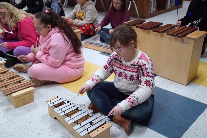 Student sitting on the floor playing an instrument.
