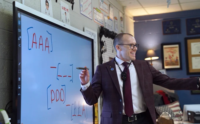 Seth Skiles smiling and standing in front of a white board.