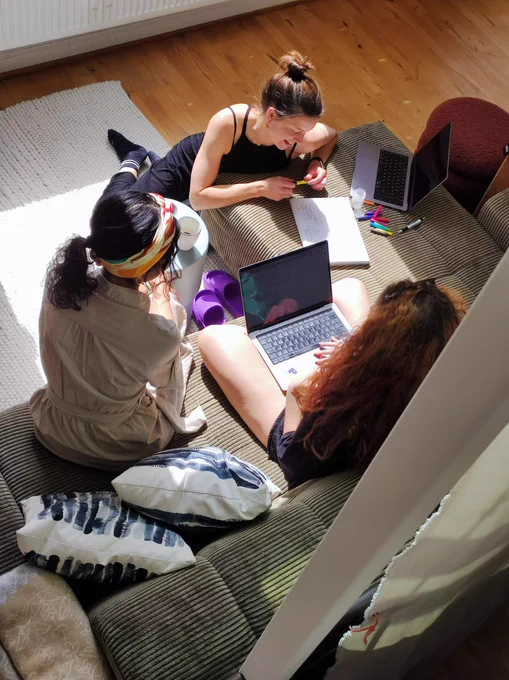 three women on a couch, surrounded by laptops and papers.