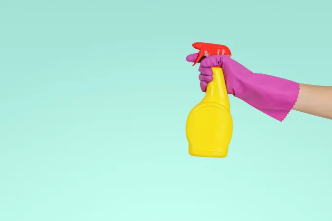 Blue background with hand in pink glove and yellow cleaning spray bottle.