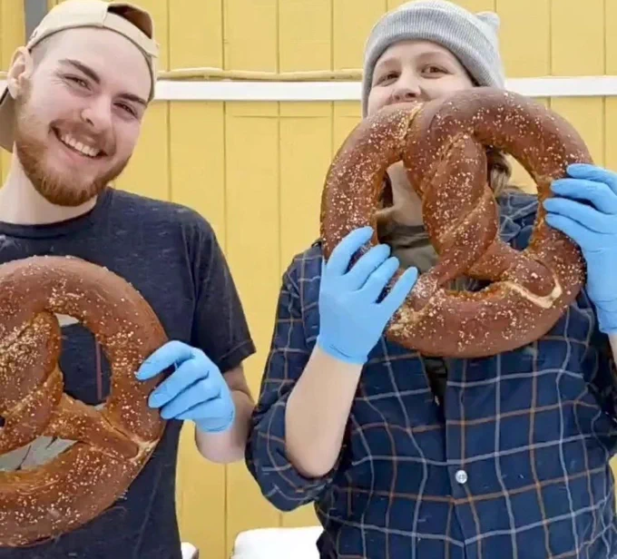 two people holding very large pretzels using both hands 