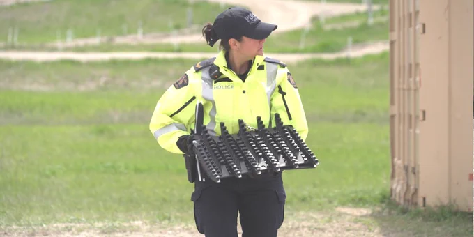 A police officer wearing a high-visibility jacket holds a Tire Deflation Device. 